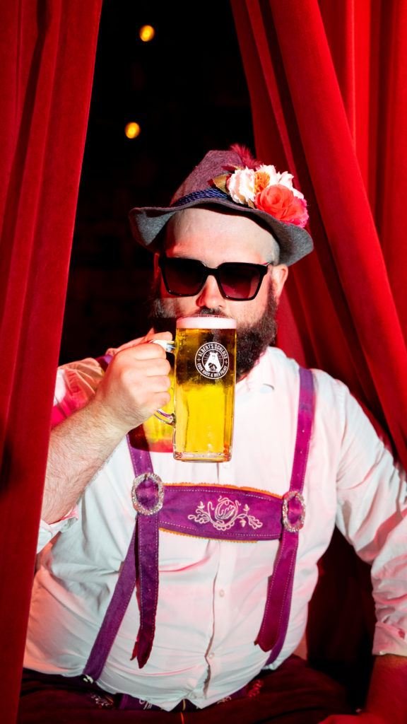 Man dressed in Bavarian attire for Oktoberfest, drinking a pint of beer.