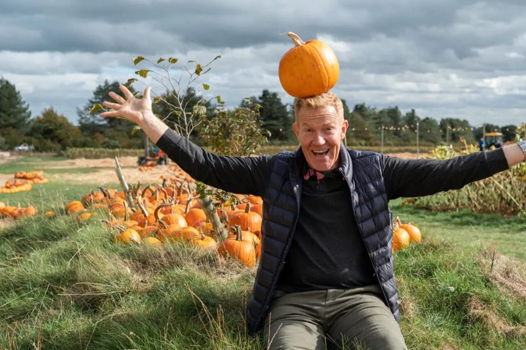 Adam Henson in the pumpkin patch, with a pumpkin on his head at Cotswolds Farm Park
